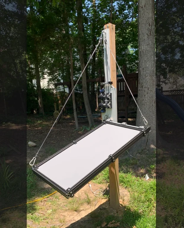 The built Dawnward prototype outdoors: a panel in an aluminium extrusion frame hanging on steel cables from a post, with an actuator and control hardware mounted on the mast above it.